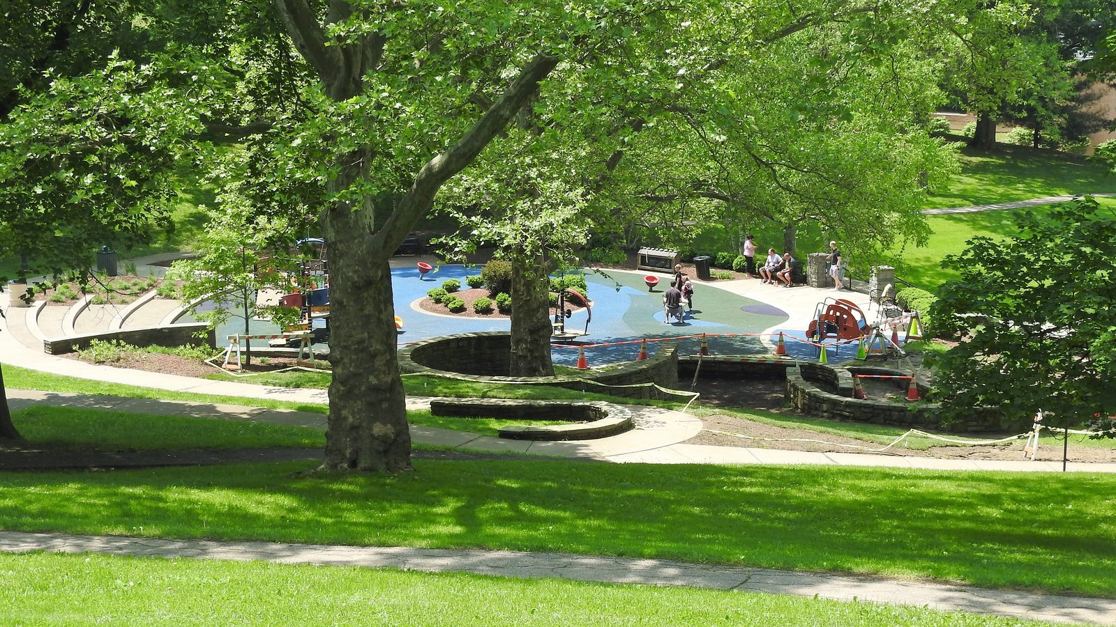A shaded neighborhood playground surrounded by large trees and lawn, similar to the play areas at H. Carroll Brooke Park in Glenside, Pennsylvania